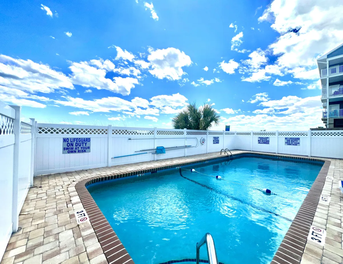 A sparkling swimming pool framed by a secure fence and open skies above, offering space for swimming, sunbathing, and group relaxation. The cheerful, communal setting is ideal for enjoying sunny days together.