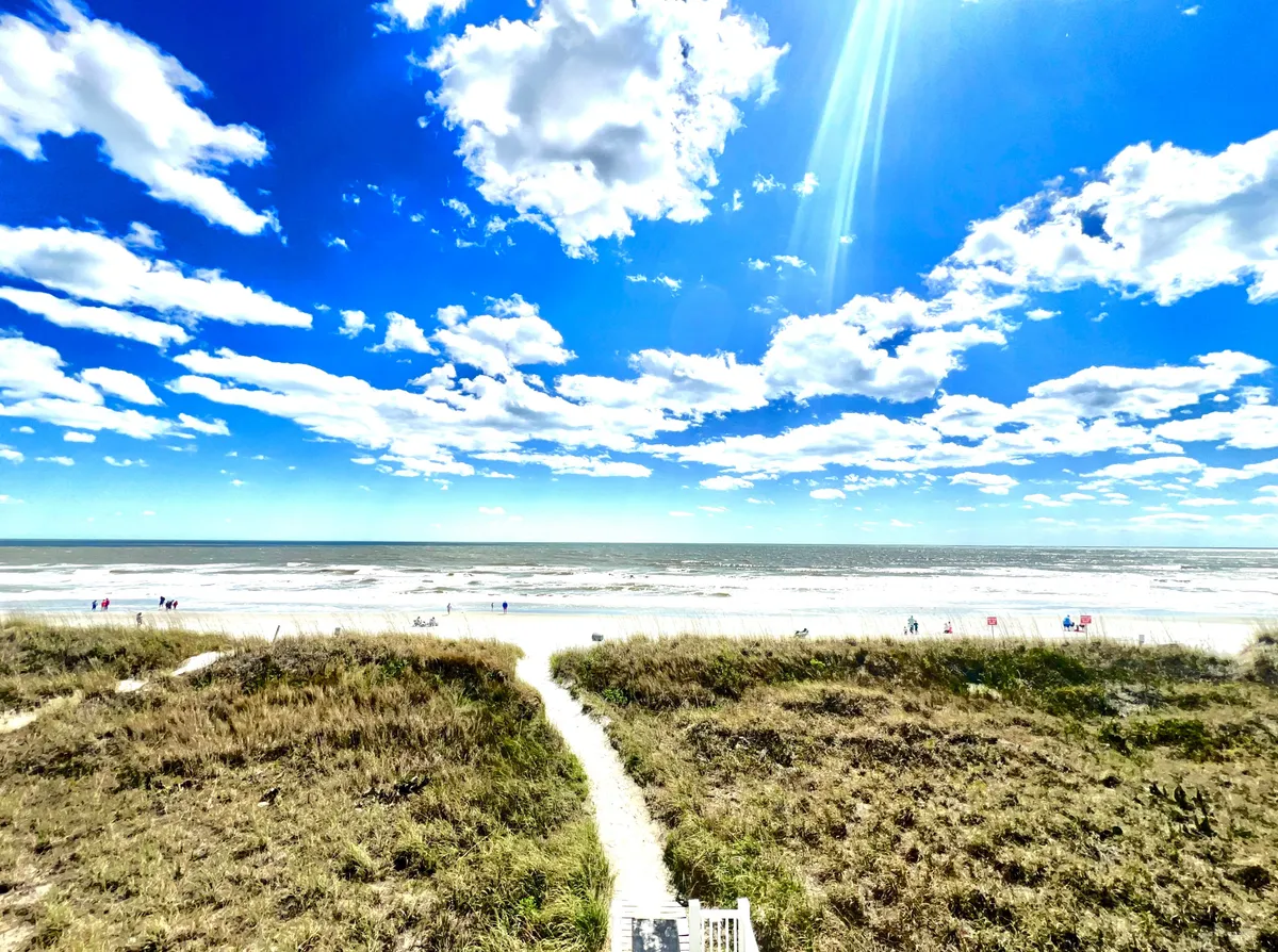 A stunning view of Cherry Grove Beach with soft sands leading to the gentle waves of the ocean, under a serene sky scattered with clouds. The pathway invites visitors directly onto the beach, setting the perfect scene for romantic strolls or sunset picnics.
